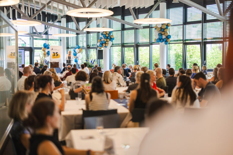 Ein mit Ballons festliche geschmückte Saal, im Hintergrund eine Bühne mit Rednerin und zuhörende Mitarbeitende - Foto: Philipp Kirschner