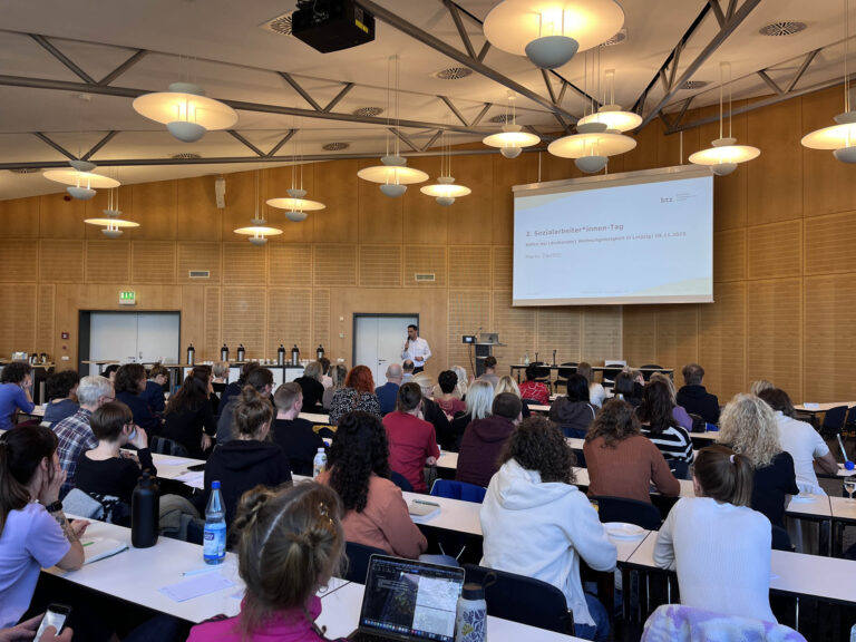 Begrüßung der Gäste zum 2. Sozialarbeiter*innen-Tag in der Aula des BFW Leipzig. Alle Gäste haben sich bereits auf ihre Plätze begeben und schauen interessiert zum Redner nach vorn.