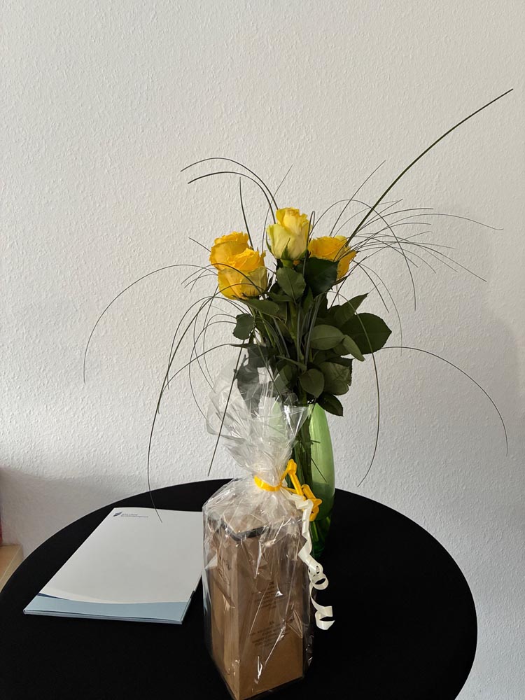 Symbolbild: Ein Strauß gelber Rosen steht mit einer Zeugnismappe und einem Geschenk auf einem Tisch