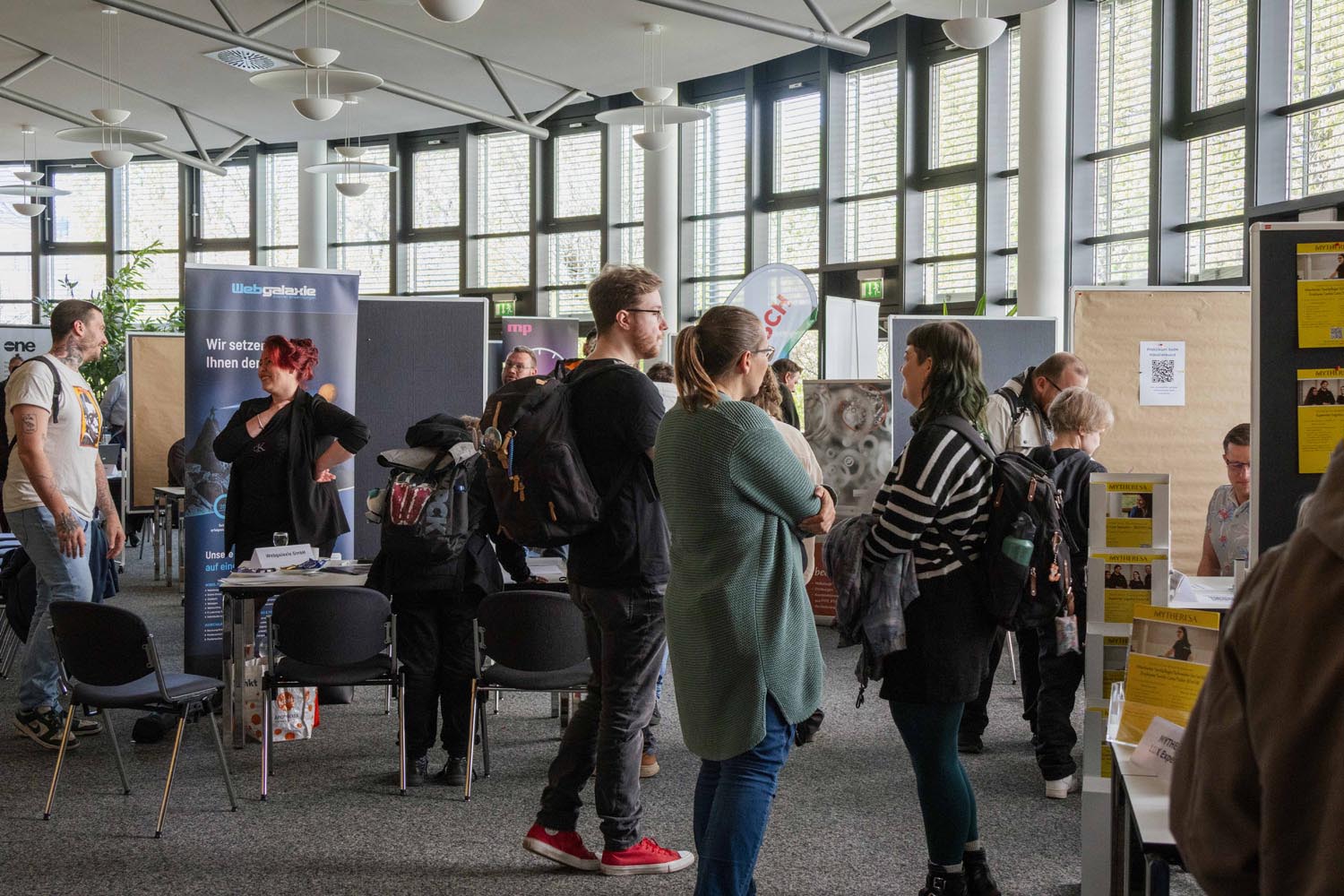 Eine Gruppe an Teilnehmenden steht zusammen am Eingang der Jobmesse und schaut auf die verschiedenen Stände der Unternehmen.