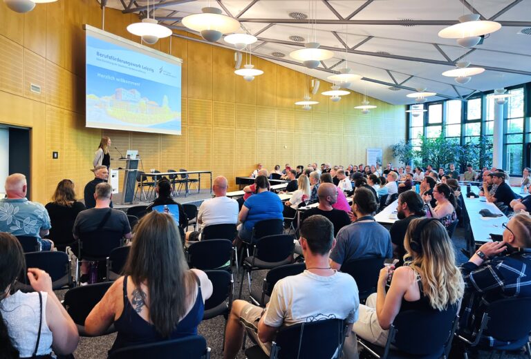 118 Personen sitzen zusammen in der großen Aula des Berufsförderungswerkes und hören sich die Einführungsveranstaltung an.