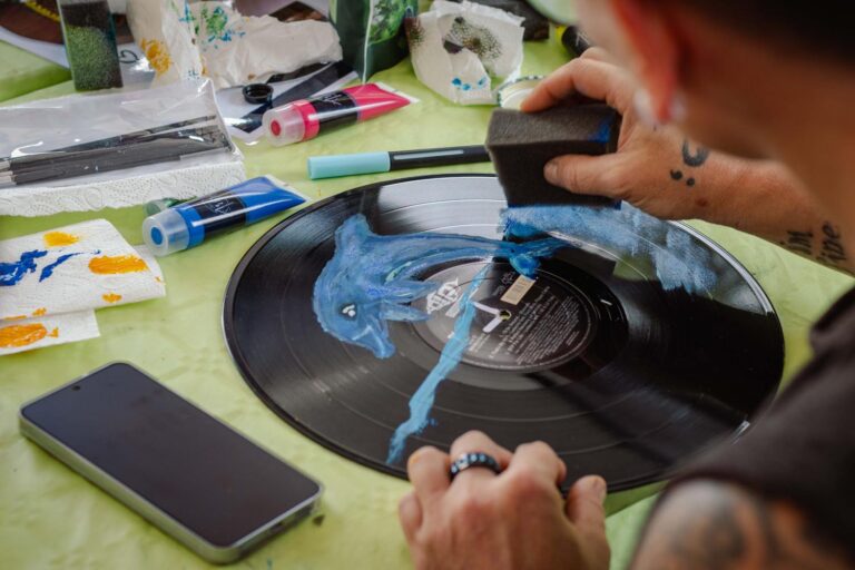 Person bemalt eine Wanduhr aus einer alten Schallplatte. Motiv: blauer Delfin.