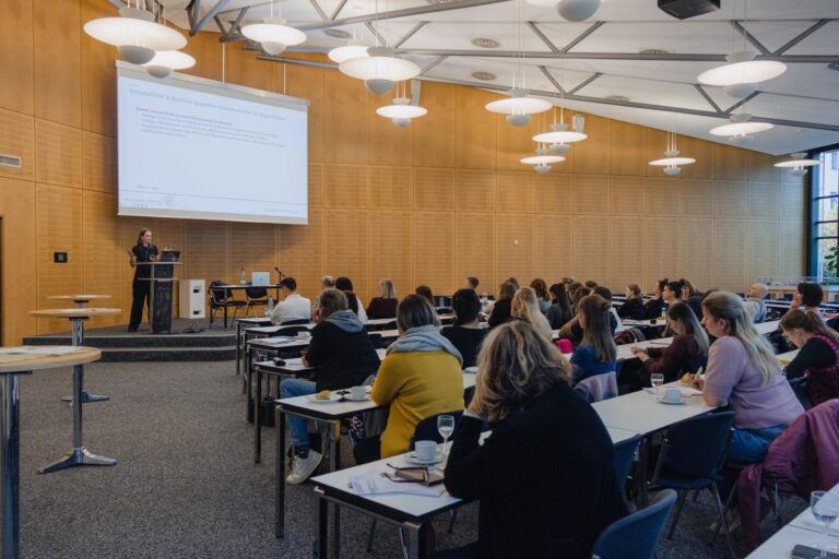 Seitlicher Blick in die Aula auf die Gäste und die Referentin: Sozialarbeiterinnen lauschen zum 3. Sozialarbeiterinnen-Tag im BFW Leipzig den Fachvorträgen in der Aula.