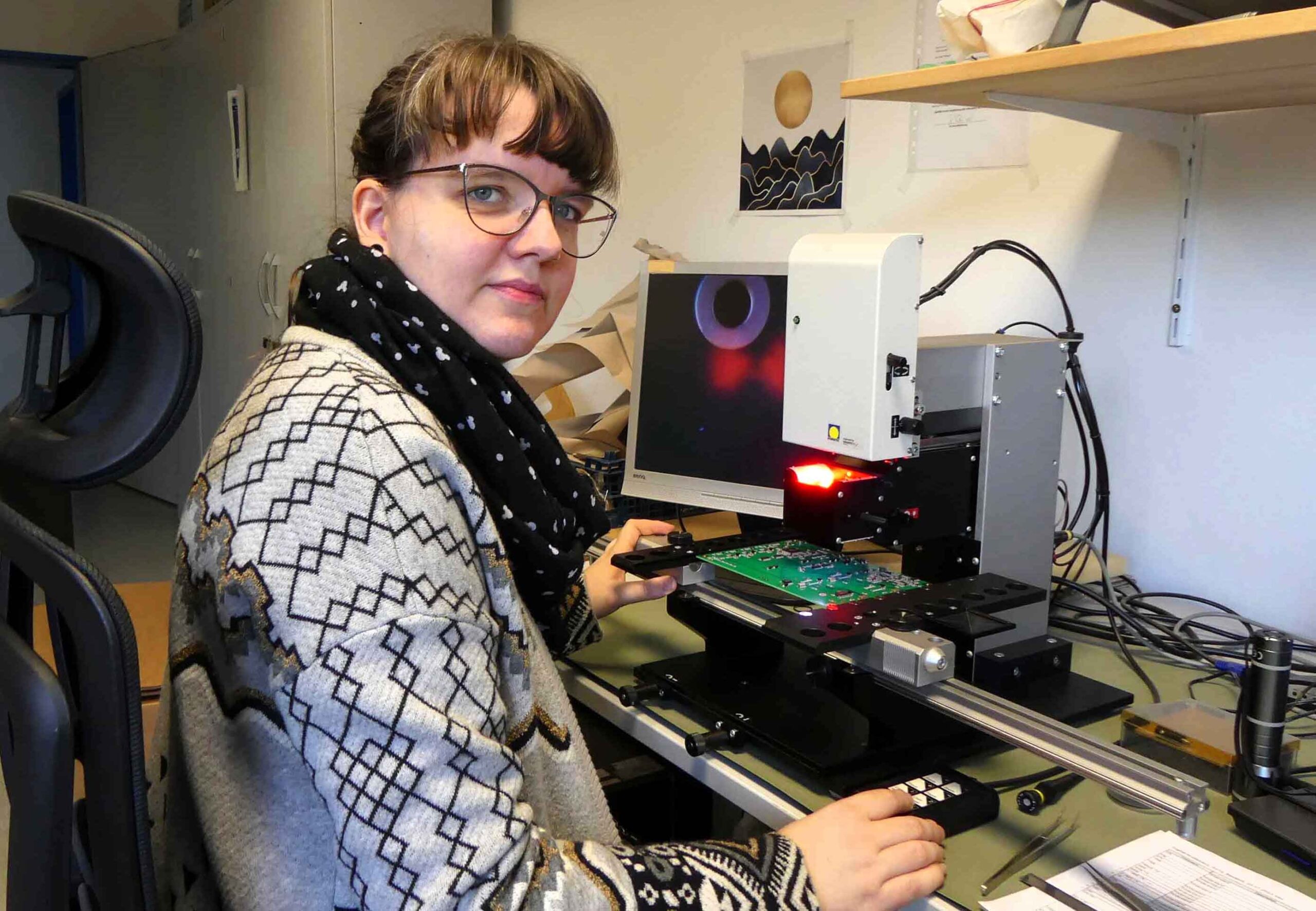 Eine weibliche Elektronikerin sitzt an einem Schreibtisch und prüft Platinen auf ihre Tauglichkeit.